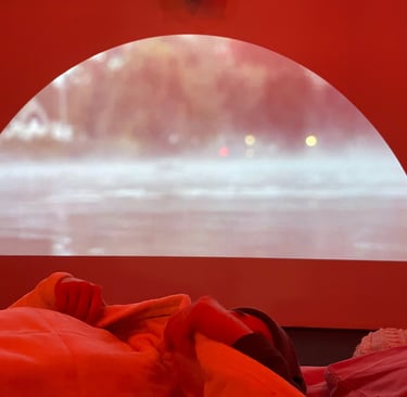 Person lies in bed under a blanket with a thermal lake projection on a half-moon screen behind them.