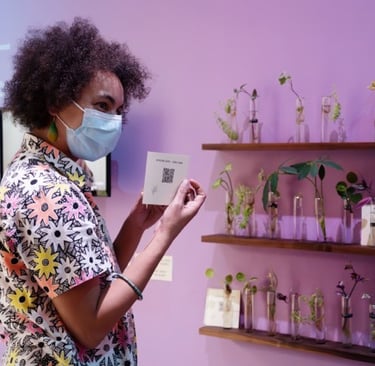 A woman holds a plant care guide in front of a wall full of plant cutting propagation tubes