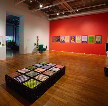 Vue de l’exposition avec divers objets sensoriels, caisses de lait et affiches tactiles.