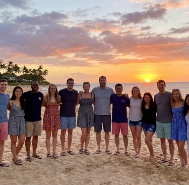 A group of people gathered together by a beach with a sunset