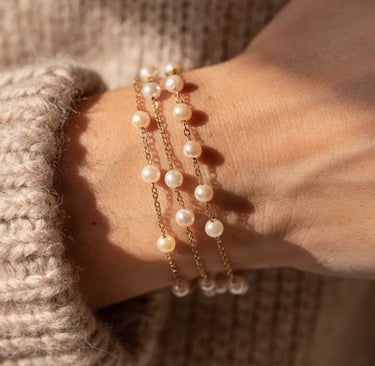 Elegant woman's wrist wearing three delicate 14k gold chain bracelets with cultured white pearls.