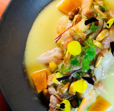 Ceviche Nikkei com peixe branco, camarão, milho crocante, batata-doce e flores comestíveis em um prato fundo escuro