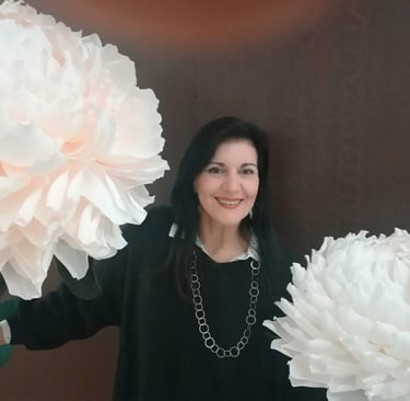 Clara Mennella sorride tra grandi fiori scenografici durante un evento legato al mondo del food & wine.