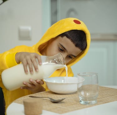Bambino versa il latte in una ciotola durante la colazione