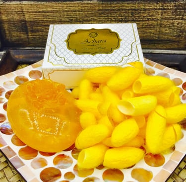 Handmade Achara luxury silk soap bar next to yellow silkworm cocoons on a mosaic plate.
