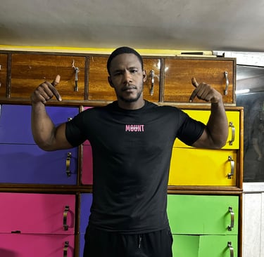 A fit man in a black Mountfit workout shirt posing in front of colorful gym lockers.