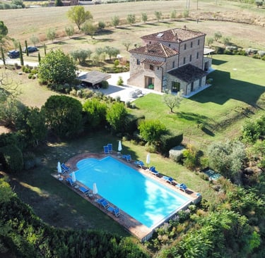 Aerial view of a luxury stone villa in Tuscany with a private swimming pool and lush garden.