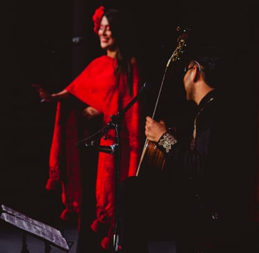 A Spanish flamenco dancer in a red shawl performs on stage with a live acoustic guitarist.