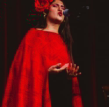 Female singer performing on stage in a red embroidered shawl and floral hair accessory.