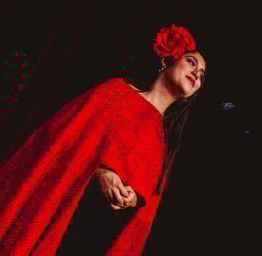 A female singer wearing a red flower in her hair and a traditional patterned red shawl performing on stage.