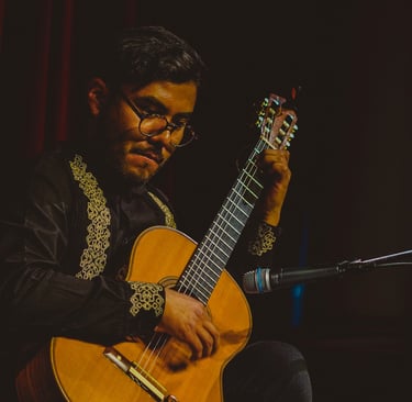 Classical guitarist in an embroidered shirt performing a solo acoustic set on stage.