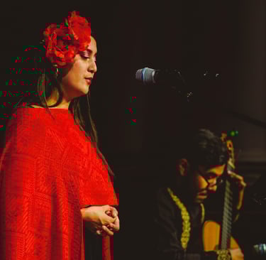 Female singer in a red floral headpiece performing live with a Spanish acoustic guitar player.