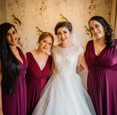 Smiling bride in a white lace wedding gown posing with bridesmaids in plum-colored dresses.