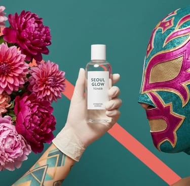 Seoul Glow hydrating toner bottle held by a gloved hand next to pink dahlias and a luchador mask.