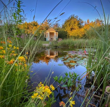 A scenic garden pond with water lilies reflecting a small wooden gazebo at sunset.