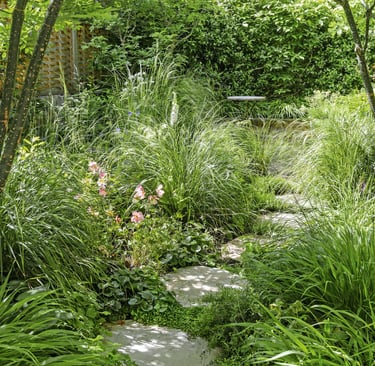Lush garden landscape featuring a stone stepping path surrounded by ornamental grasses and pink flowers.