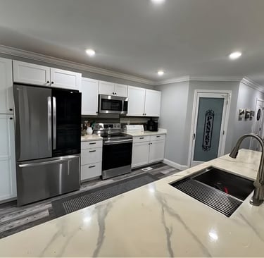 Modern kitchen with white cabinets, stainless steel appliances, and a marble island with a sink.