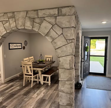 Rustic dining room with a stone archway, dark wood table, and grey laminate flooring.