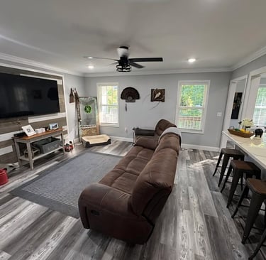 Modern living room with brown reclining sofa, wood accent wall, and grey vinyl plank flooring.