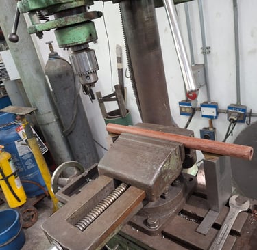 Una prensa de taladro sujetando un tubo de madera en un taller listo para perforarlo