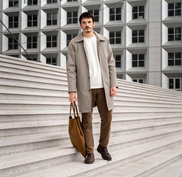 Portrait d’un homme élégant marchant sur les marches de La Défense, sac à la main, dans un décor urbain graphique et structur