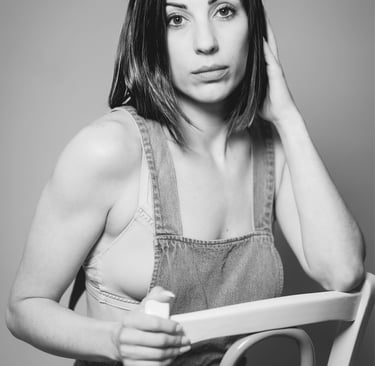 Portrait en noir et blanc d’une femme assise sur une chaise, en salopette, le regard franc.