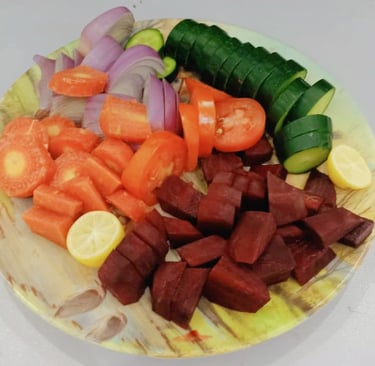 Colorful fresh vegetable salad with sliced cucumber, tomatoes, red onions, carrots, beetroot, and lemon on a plate..
