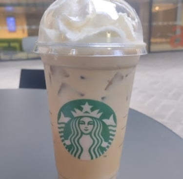 Iced caramel macchiato with whipped cream in a Starbucks takeaway cup on a black table, perfect summer coffee beverage