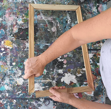 a person holding a wooden frame with a painting on it