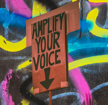 A sign reads "Amplify your voice" over a noisy graffiti background (communication coaching)