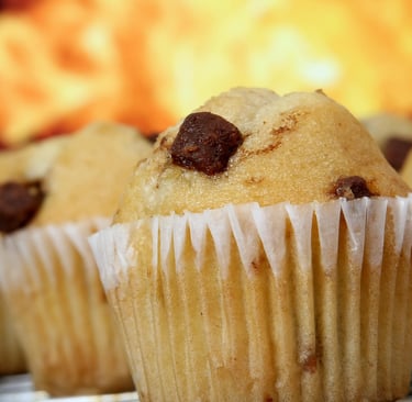Close-up of freshly baked chocolate chip muffins on a cooling rack with a warm background.