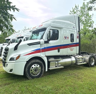 Camión AFH Logistics con remolque aparcado junto a césped y árboles