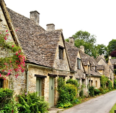 Historic stone weaver cottages with gabled roofs and flowers at Arlington Row in Bibury, Cotswolds.