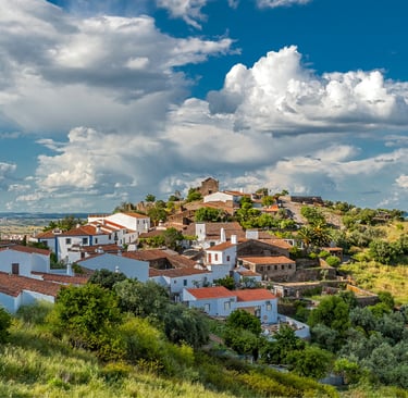 Panoramic view of white houses in a traditional Portuguese village under a cloudy blue sky.