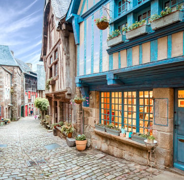 Charming cobblestone street in Dinan, France with blue half-timbered houses and flower boxes.