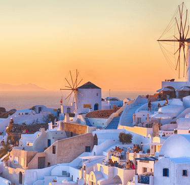 Traditional white windmills and houses in Oia, Santorini overlooking the Aegean Sea at sunset.