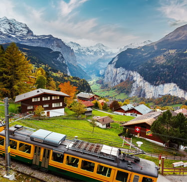 Yellow Swiss train traveling through Wengen village overlooking the Lauterbrunnen valley and Alps.