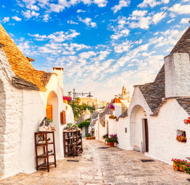 Traditional white trulli houses with conical stone roofs in a scenic street of Alberobello, Italy.
