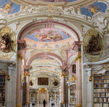 Ornate Baroque architecture of the Admont Abbey Library featuring ceiling frescoes and gold accents.