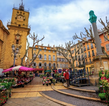 Outdoor flower market in Aix-en-Provence square with historic clock tower and colorful French buildings.