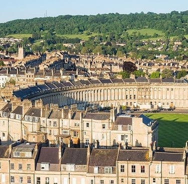 Aerial view of the historic Royal Crescent in Bath, England, featuring Georgian architecture and lush green hills.