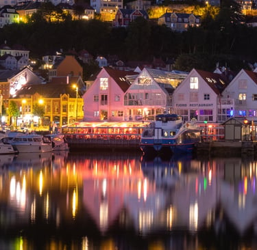 Night view of Bergen, Norway's historic harbor with illuminated waterfront buildings and colorful reflections.
