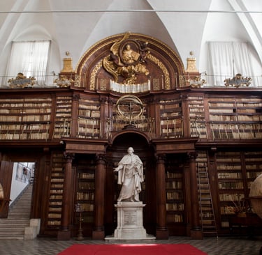 Ancient ornate library with floor-to-ceiling wooden bookshelves, marble statues, and antique globes.