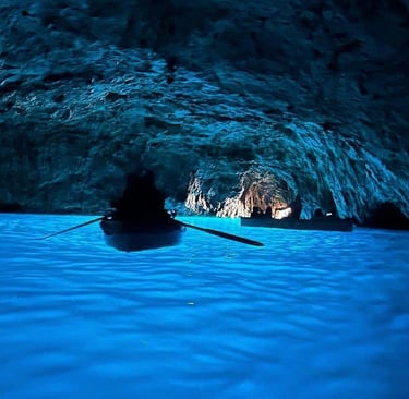 Small rowboats exploring the stunning Blue Grotto sea cave in Capri, Italy, with vibrant blue illuminated water.