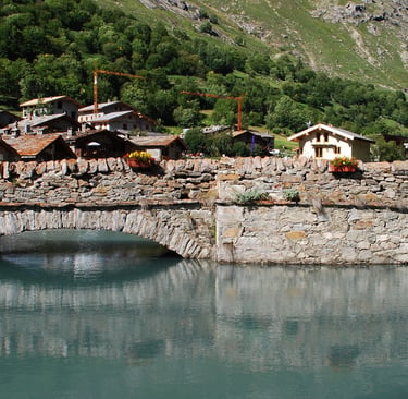 Historic stone arch bridge over a turquoise alpine river in a scenic mountain village.