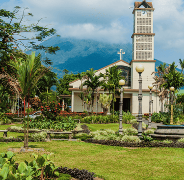 A tropical garden and church in La Fortuna with the Arenal Volcano in the background.