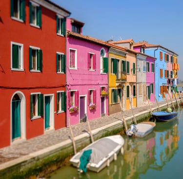Colorful houses along a canal in Burano Venice with small boats docked in the water.