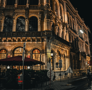 The historic Palais Ferstel building in Vienna illuminated at night with a street cafe and horse-drawn carriage.