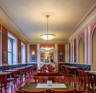 Elegant restaurant interior with red patterned wallpaper, luxury dining tables, and ornate white molding.