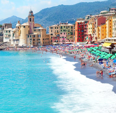 Sunny view of Camogli beach in Liguria, Italy, with colorful houses and turquoise Mediterranean waters.